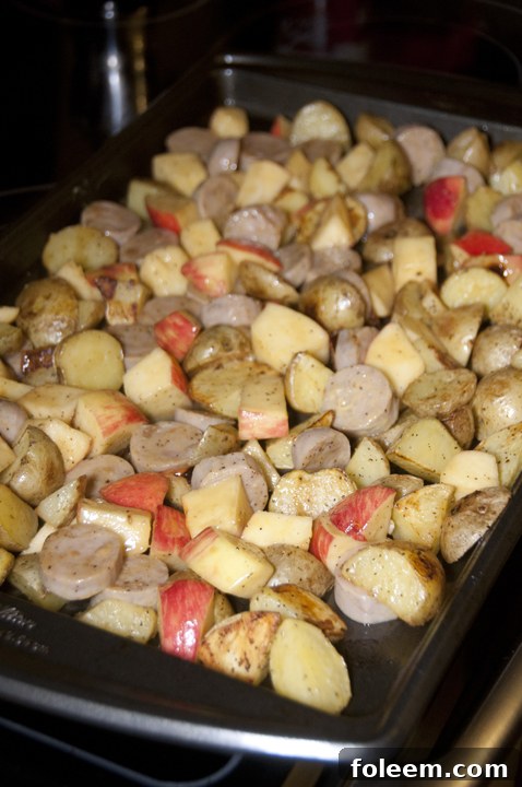 Freshly cut potatoes, apples, and chicken sausage, seasoned and ready for baking in the oven. A beautiful display of ingredients before they transform into a delicious one-pan meal.