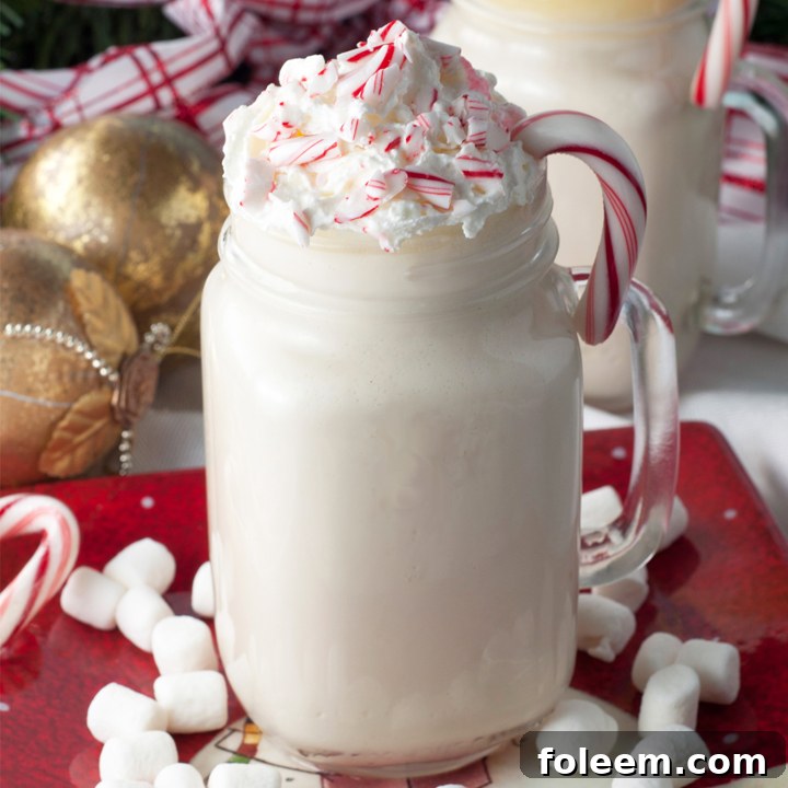 A festive holiday spread featuring Slow Cooker Snowflake White Hot Chocolate in mugs, alongside various sweet treats and garnishes.