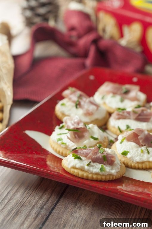 Close-up of Whipped Ricotta Prosciutto Cracker Bites, highlighting the texture of the whipped ricotta, the delicate folds of prosciutto, and the sprinkle of green chives, ready to be served.