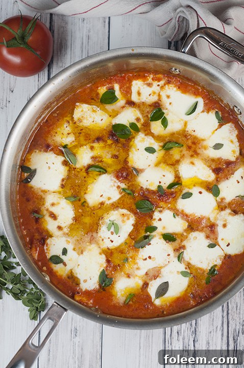 Delicious Ravioli al Pomodoro with melted fresh mozzarella cheese, ready to be served from a skillet. A perfect easy Italian one-skillet meal, garnished with fresh herbs.