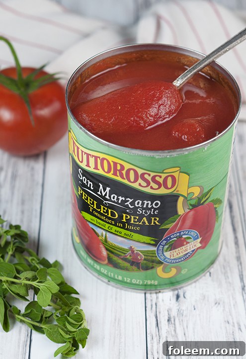 A can of Tuttorosso San Marzano Style Pear Tomatoes, elegantly displayed with fresh basil leaves and coarse sea salt, signifying premium ingredients for an authentic Italian sauce.