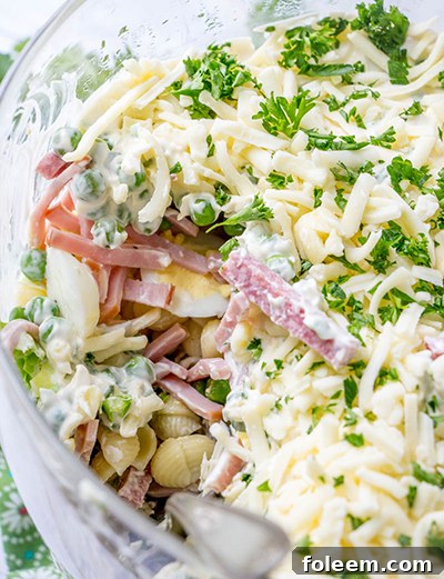 Layered salad with pasta, ham, salami, peas, and a creamy dressing.