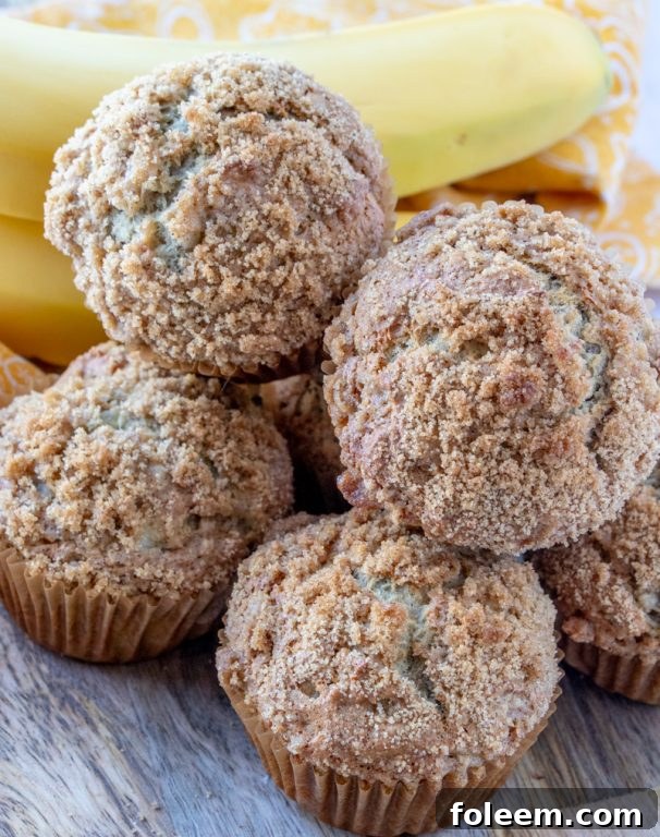Hand reaching for a freshly baked banana crumb muffin, highlighting its fluffy texture and generous crumb.