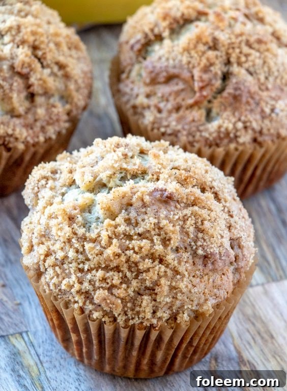 Close-up shot of a banana crumb muffin, revealing its moist interior and generous streusel topping, ready to be eaten.