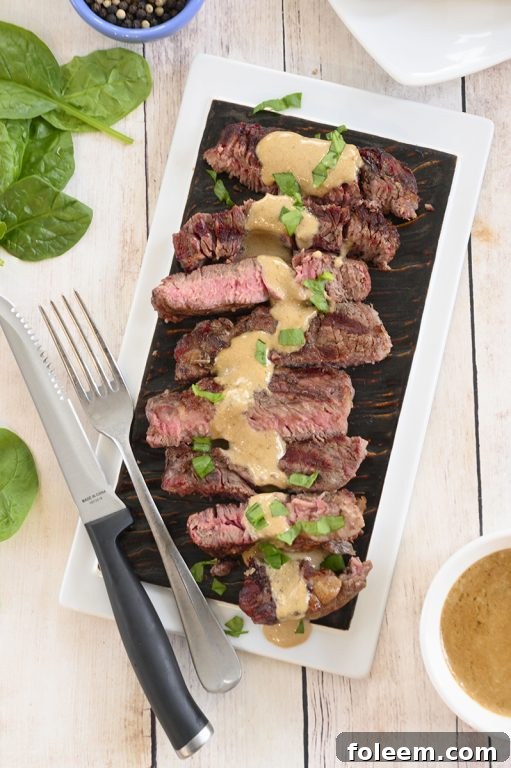 Close-up of a grilled ribeye steak resting on a cutting board, ready to be sliced, alongside a bowl of rich onion blue cheese sauce.