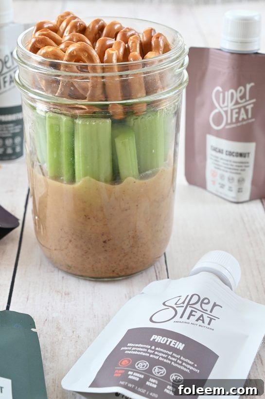 A vibrant Mason Jar Pretzel, Celery, Almond Butter Snack with SuperFat nut butter, perfect for a healthy on-the-go protein-rich energy boost.