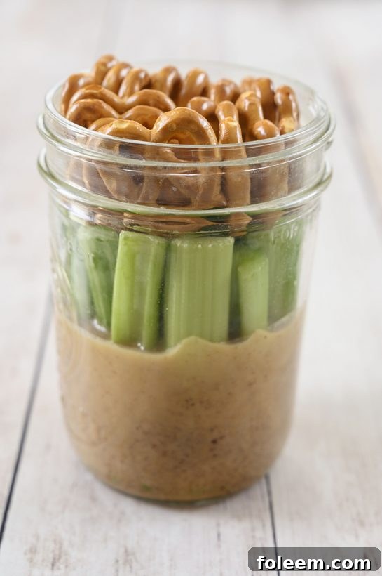 A gluten-free, vegan Mason Jar Pretzel, Celery, Almond Butter Snack featuring SuperFat nut butter, designed for a healthy protein-packed energy boost.