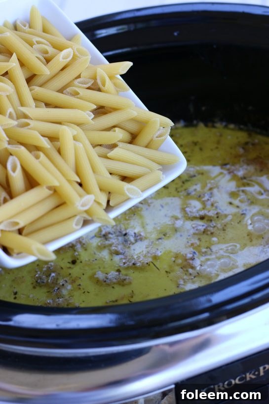 Adding penne pasta to the alfredo sauce in a crock pot.