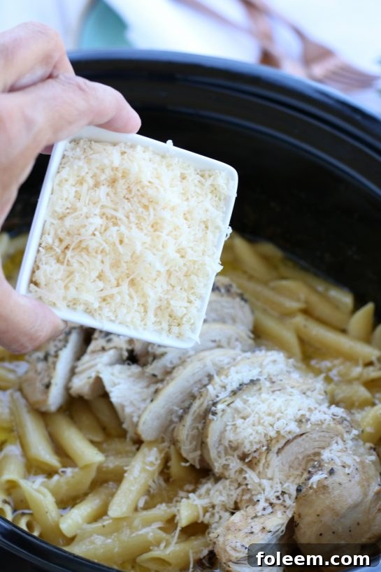 Sprinkling freshly grated Parmesan cheese on top of a chicken alfredo crock pot recipe.