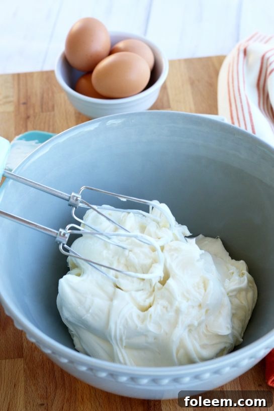 Softened cream cheese whipped with a hand mixer in a blue mixing bowl.