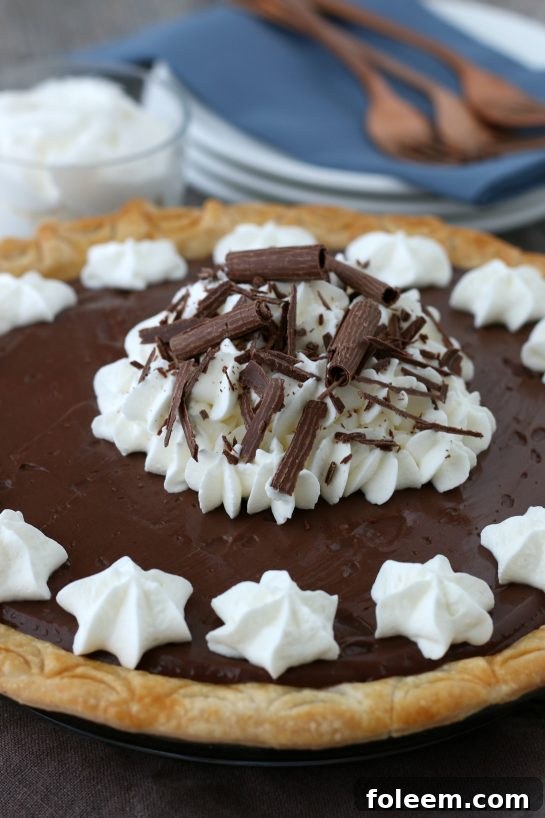 An exquisite close-up of a finished old-fashioned chocolate pie, lavishly topped with swirls of homemade whipped cream and delicate chocolate shavings, highlighting its rich textures.