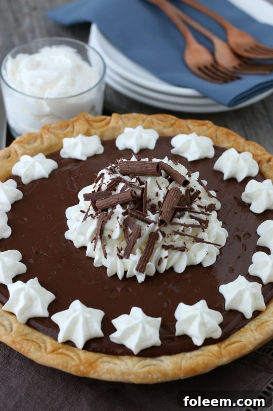 A magnificent homemade chocolate pie, often referred to as old-fashioned chocolate pie, made with luscious homemade chocolate pudding and elegantly topped with swirls of whipped cream, ready to be served and enjoyed. A picture of dessert perfection.