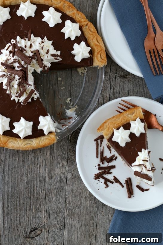 Top down view of a glorious homemade chocolate pie with one slice already served on a pristine white plate, showcasing its decadent layers of filling and crust.