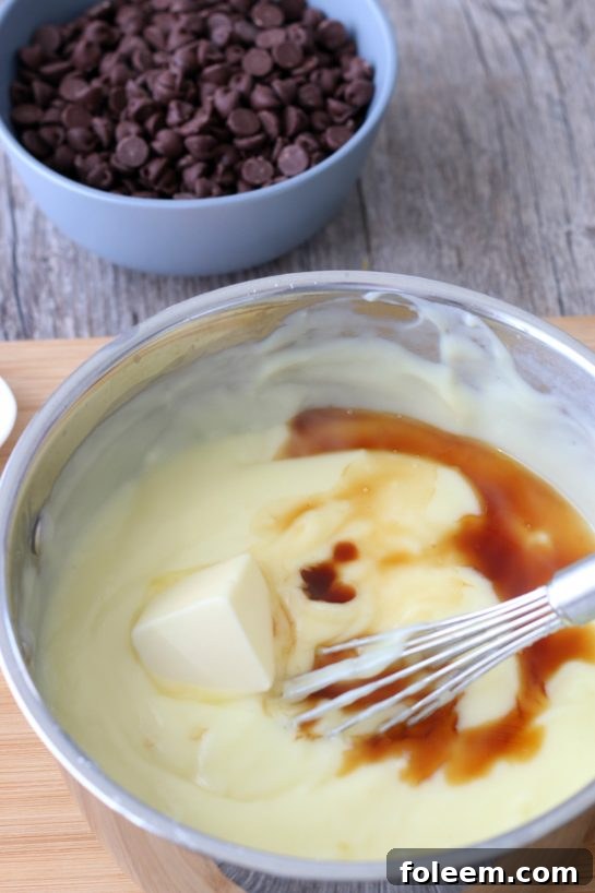 A crucial step in making the chocolate pie: showcasing the addition of rich butter and aromatic vanilla extract to the warm, glossy pudding mixture.