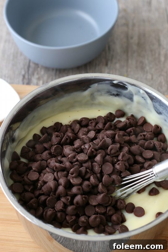 Close-up shot of decadent chocolate chips being gently stirred into the freshly made, warm homemade chocolate pudding mixture, a key step in creating the pie filling.
