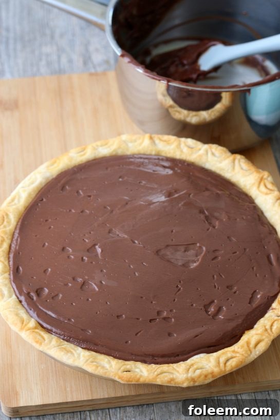 A pristine old-fashioned chocolate pie, perfectly prepared and cooling, patiently waiting to be chilled and then graciously served to eager guests.