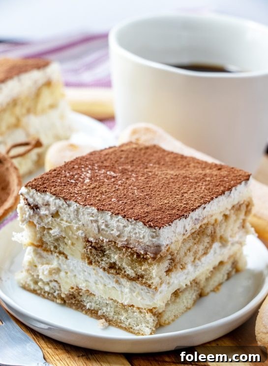 A beautifully layered slice of Grandma's Tiramisu, showcasing coffee-soaked ladyfingers, creamy mascarpone, and a dusting of cocoa powder.