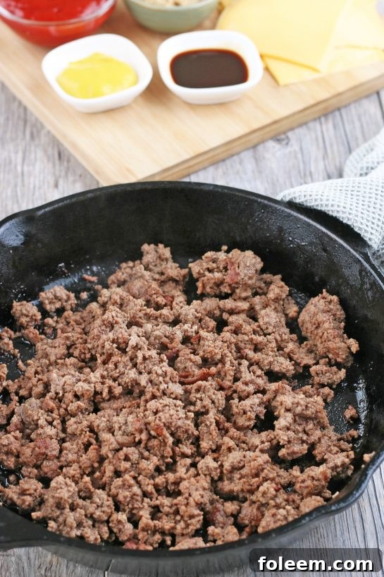 The first crucial step in making cheeseburger biscuit bites: cooking and crumbling the ground beef in a skillet.