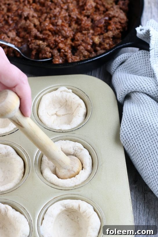 The process of forming the biscuit cups for our delicious cheeseburger bites in a muffin tin, ensuring a perfect base for the filling.