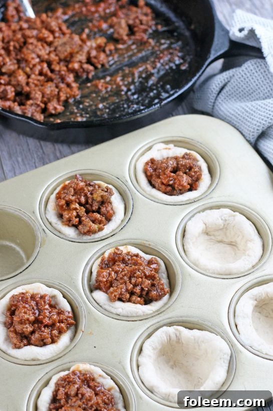 Filling the perfectly formed biscuit cups with our savory meat mixture, a key step in preparing the delicious cheeseburger cups.
