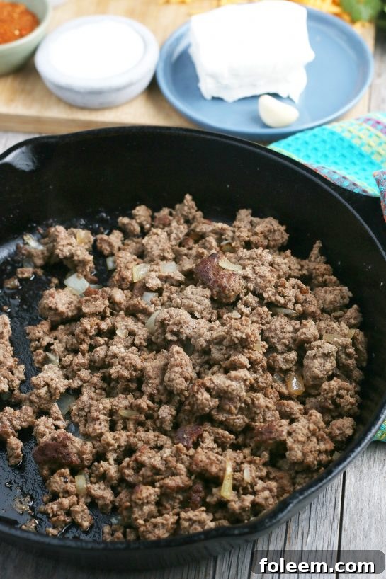 The first step in preparing taco pasta: ground beef and diced onions are sizzling in a large skillet, browning to perfection.