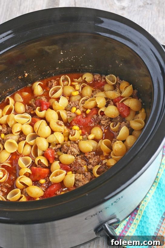 The pasta has been added to the slow cooker taco pasta mixture and is now being stirred to combine all ingredients before the final cooking phase.