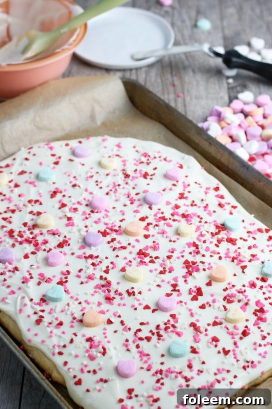 The process of adding conversation hearts to the melted almond bark spread over the baked sugar cookie, completing the festive decoration.
