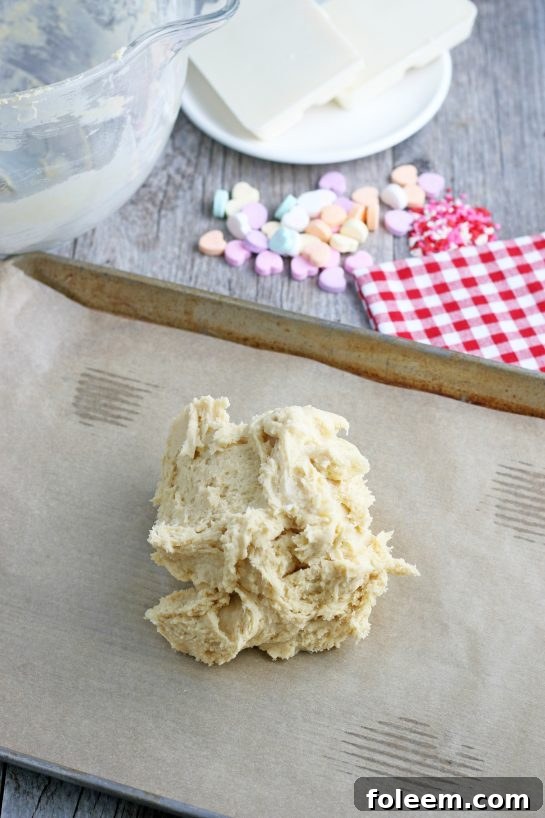 Now the ball of sugar cookie dough is placed on a lined cookie sheet, ready to be pressed evenly and baked to form the base of the conversation heart cookies.