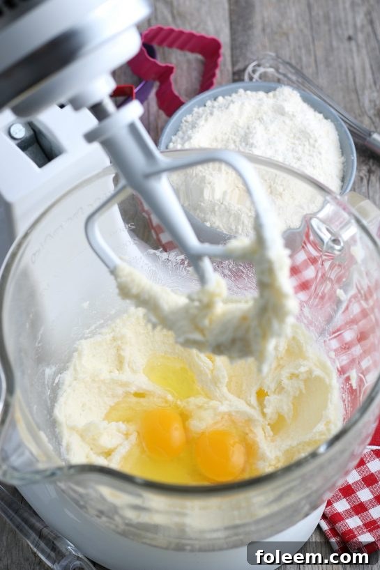 The crucial step of adding eggs to the light and fluffy butter-sugar mixture, moving closer to completing the dough for decorated sugar cookies.