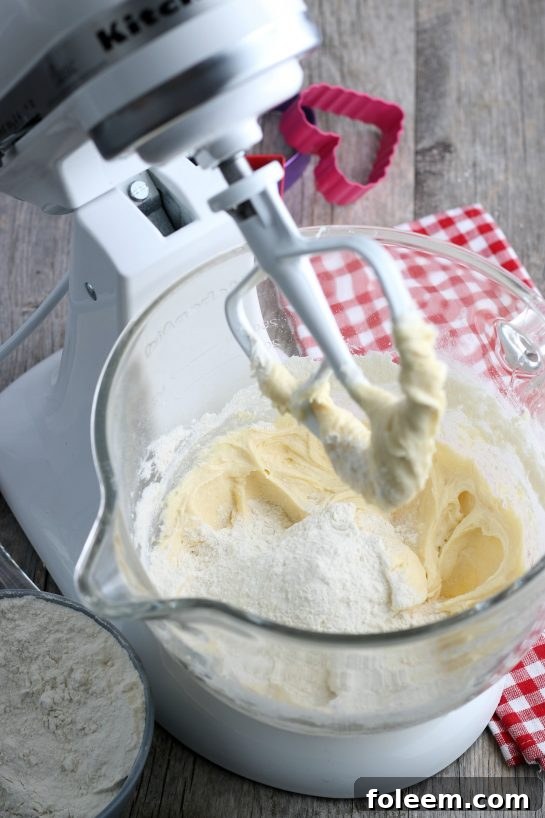 Dry ingredients are being incorporated into the stand mixer, signifying the final stages of preparing the batter for delicious Valentine's cookies.