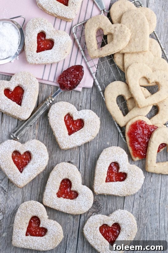 A top-down view of beautifully decorated heart-shaped Linzer cookies, dusted with powdered sugar and filled with vibrant red jam, ready to be enjoyed.