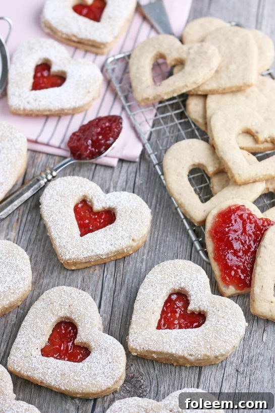 A close-up of the finished Linzer cookies, with jam being spread onto the bottom halves and the top cookie layers carefully assembled.