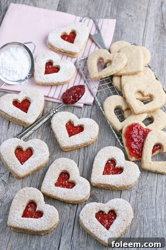 A delightful scene featuring finished heart-shaped Linzer cookies, with more being assembled in the background, showcasing the baking process.