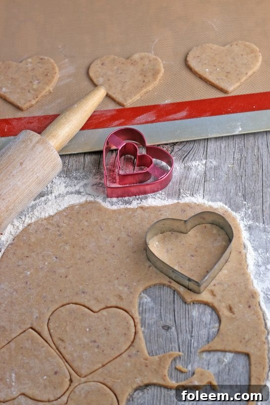 Heart-shaped Linzer cookie dough being cut with cookie cutters and carefully placed onto baking sheets, ready for the oven.