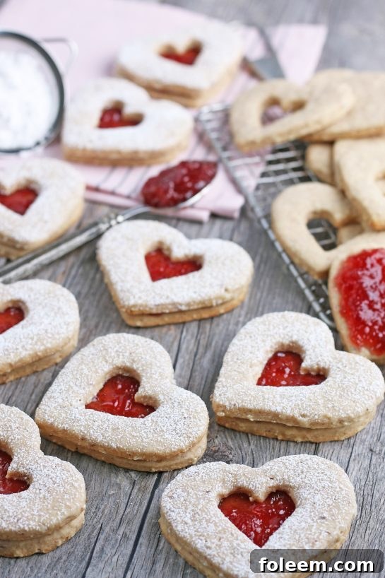 A close-up view of finished Linzer tart cookies, delicately dusted with powdered sugar, showcasing their beautiful heart shapes and tempting jam centers.