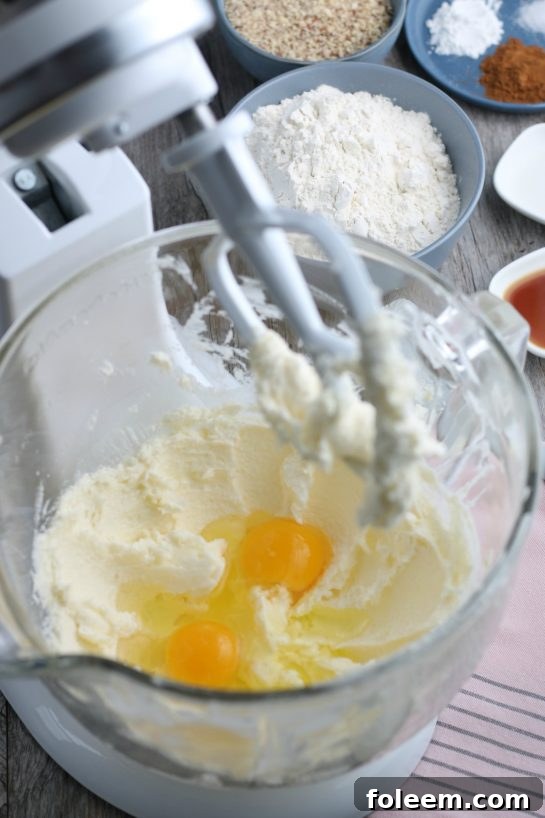 A view inside the stand mixer as eggs are carefully added to the Linzer tart cookie batter, ensuring a smooth and cohesive mixture.