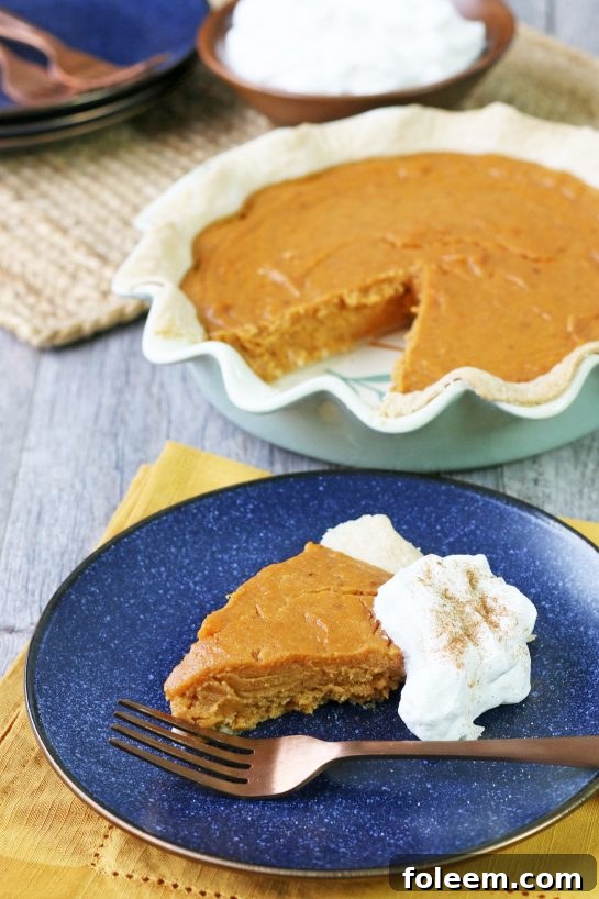 A perfect slice of sweet potato pie, topped with a generous swirl of homemade spiced whipped cream, on a white plate ready to be enjoyed.