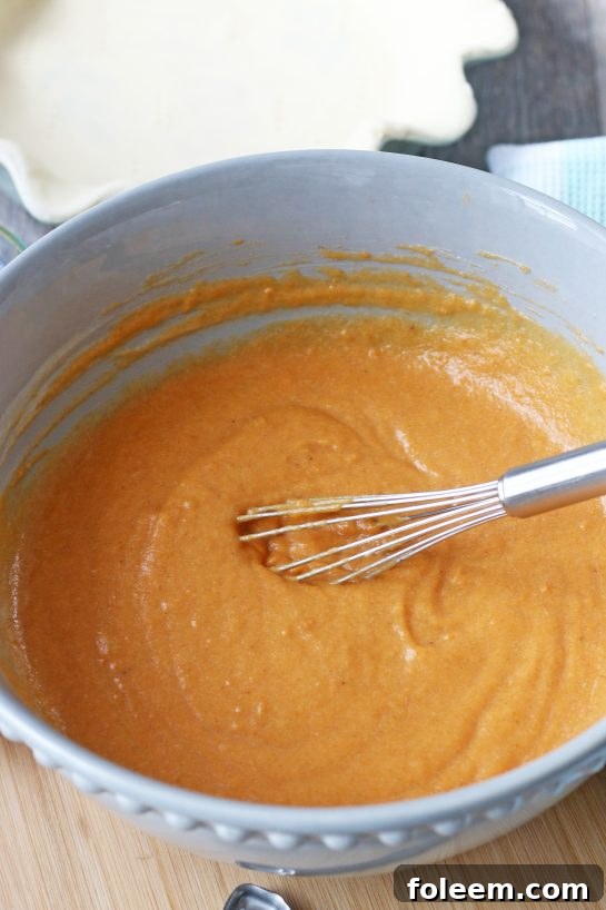 A close-up view of a serving of sweet potato pie with creamy whipped topping, ready for a delectable bite.