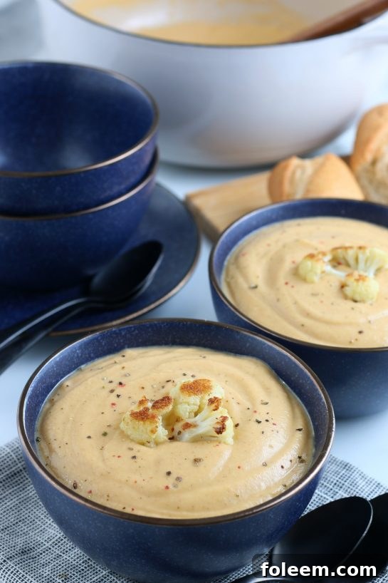 A closer view of the finished Roasted Cauliflower Soup in a ceramic bowl, beautifully garnished with roasted cauliflower florets and a sprinkle of fresh herbs. It's perfectly smooth and inviting.