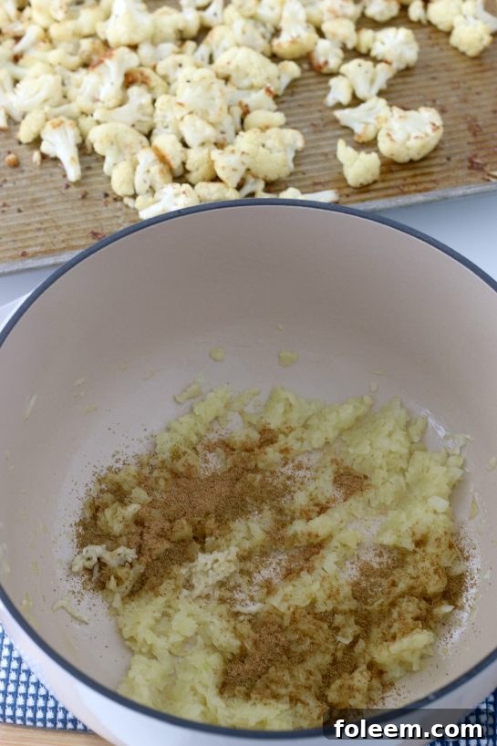 A vibrant mix of roasted cauliflower florets, golden brown and perfectly caramelized, sprinkled with fresh green herbs. The seasoning is visible, indicating rich flavor.