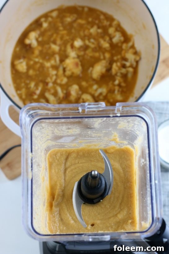 The process of blending the roasted cauliflower and broth into a smooth, creamy soup, captured with a view inside the blender as the mixture swirls.