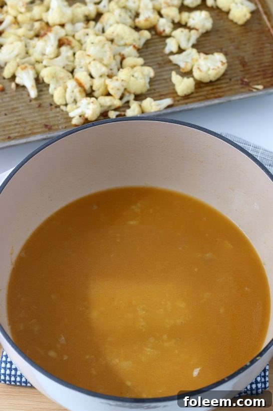 A large pot filled with a rich, aromatic broth, infused with spices and ready to receive the roasted cauliflower, highlighting the flavorful liquid base of the soup.