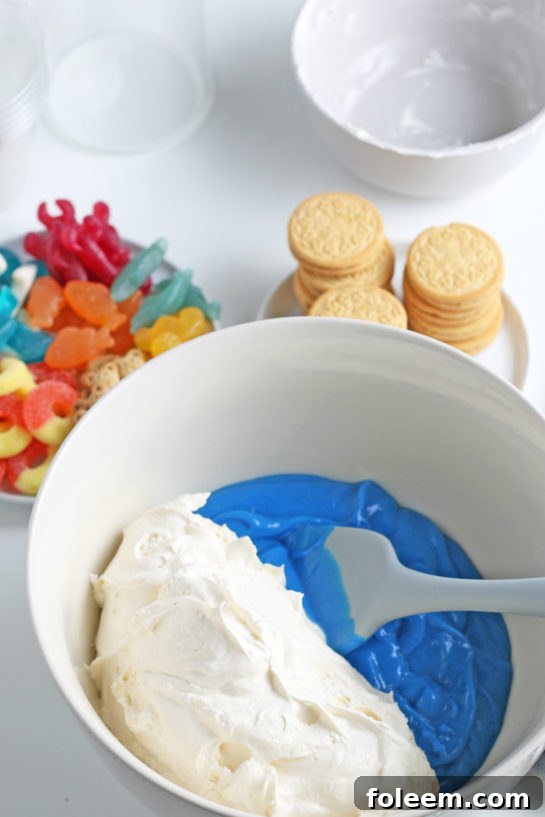 Adding the whipped topping to the blue Jello to the bowl to make beach sand pudding cups recipe