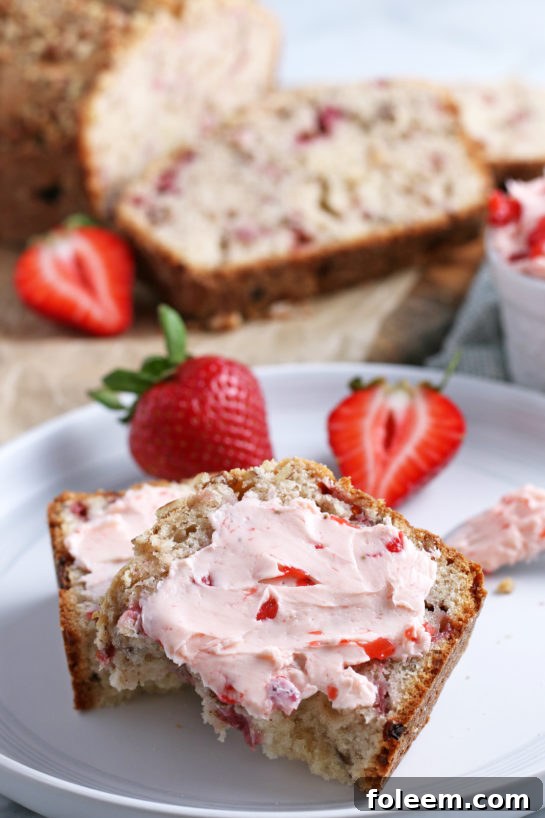 A tantalizing close-up of a slice of strawberry bread generously spread with fresh strawberry cream cheese, highlighting its fluffy texture and rich, fruity taste.