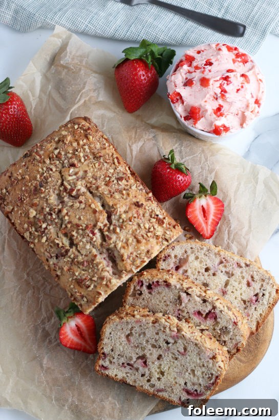 A beautiful overhead view of a freshly baked loaf of strawberry bread, sliced into perfect portions, revealing the delicate pink hue and chunks of real strawberries throughout.