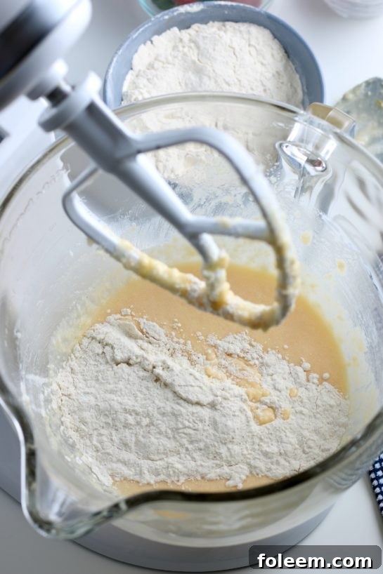 The dry ingredients are slowly being added to the stand mixer bowl, gradually coming together with the wet mixture to form the perfect strawberry bread batter.