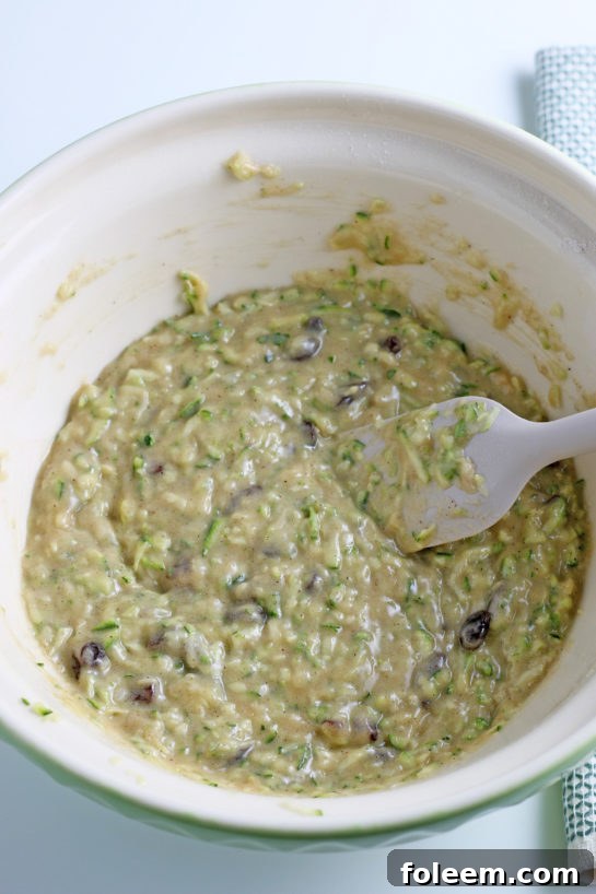 The final stage of mixing the wet and dry ingredients together for the zucchini muffins, creating a rich, textured batter ready for baking.