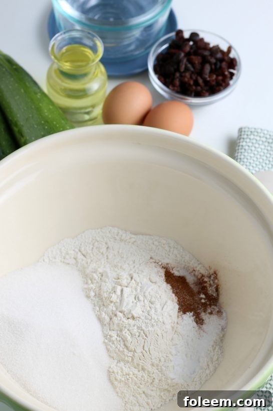 Dry ingredients, including flour, sugar, baking powder, baking soda, salt, and fragrant cinnamon, being whisked together in a mixing bowl for the zucchini muffins recipe.