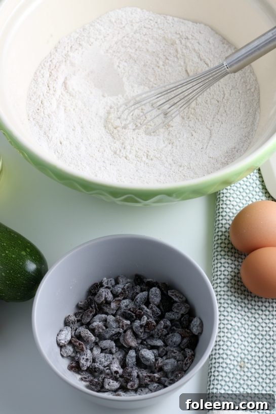 Plump raisins being added to the zucchini muffin batter in a mixing bowl, ready to be gently folded in for a touch of sweetness and chewiness.