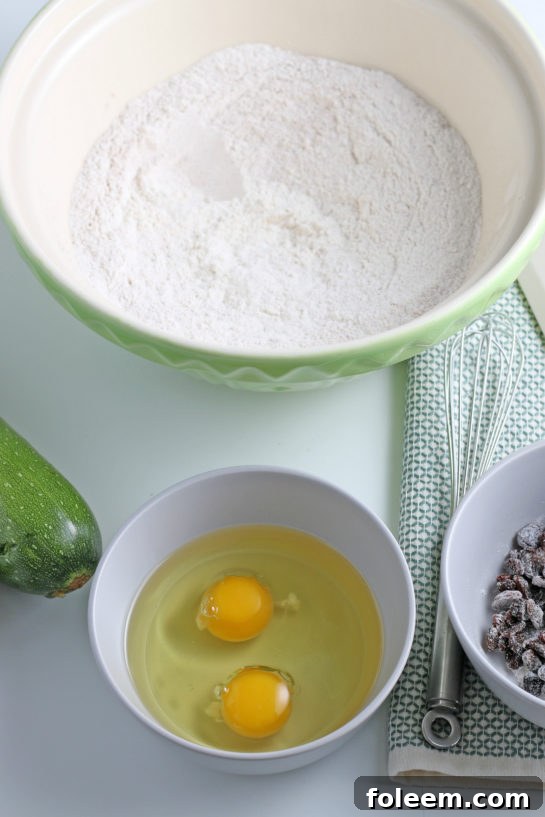 Fresh eggs being cracked into a small mixing bowl, ready to be whisked with oil as part of the wet ingredients for the super soft zucchini muffins.